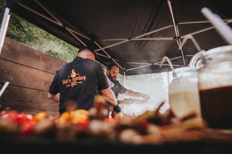 Zwei Grillmeister unter dem Pavillon, vorne frisches Gemüse und Dips