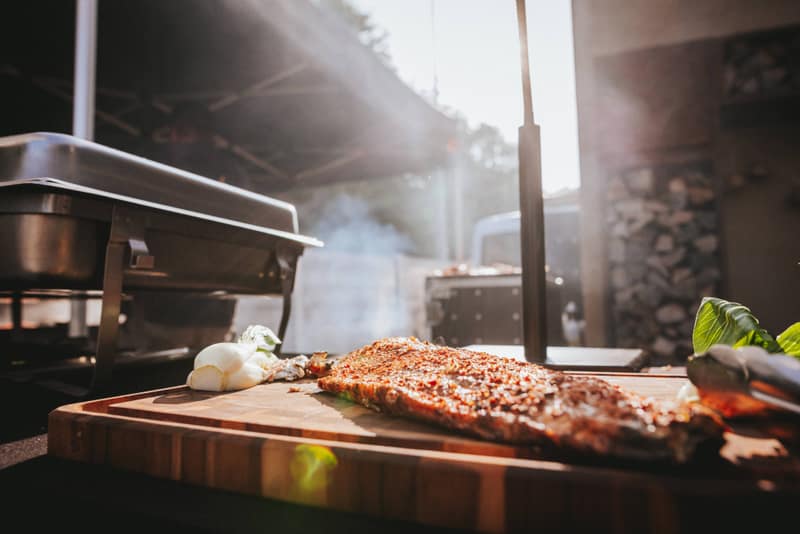 Fleisch auf dem Holzbrett, dahinter Rauch an der Buffetstation