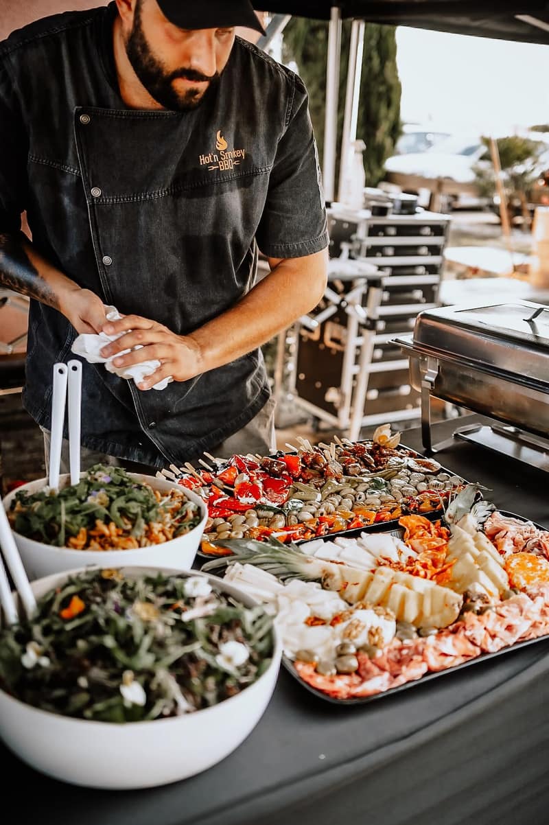 Grillmeister richtet Antipasti-Platten und Salate an