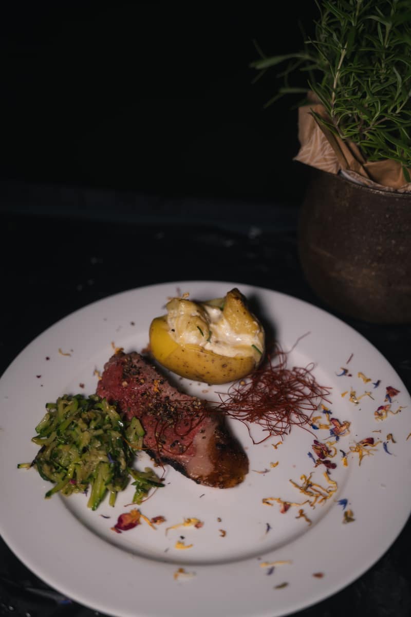Angerichteter Teller mit Steak, Ofenkartoffel und Kräutern