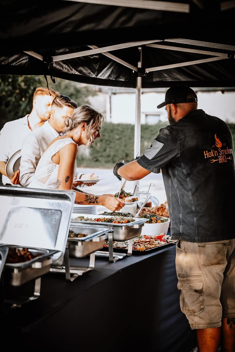 Hochzeitsgäste am Buffet, daneben der Grillmeister