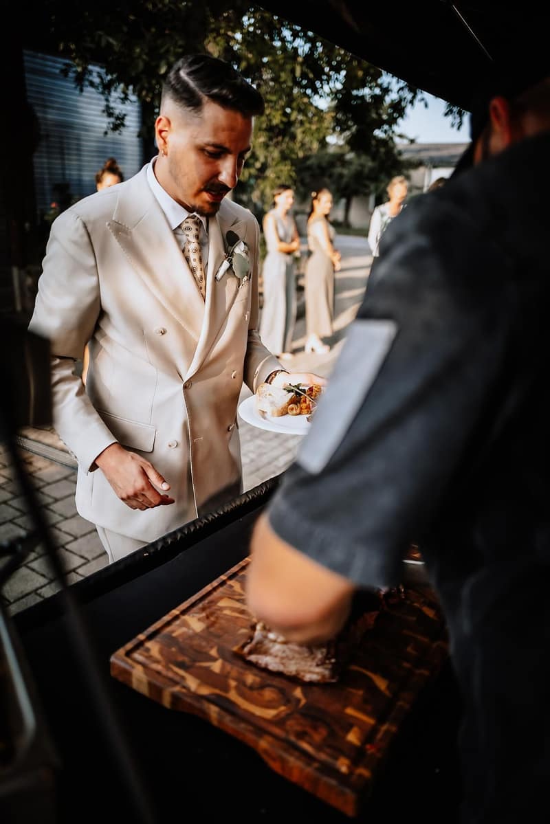 Bräutigam im hellen Anzug am Live-Grill einer Hochzeit